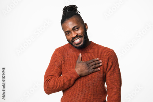 Cheerful touched with a compliment happy shy african-american young man in red sweater with dreadlocks looking at camera with toothy smile isolated in white background photo