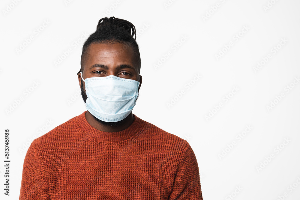 Pandemic illness concept. African-american young man wearing protective face mask against coronavirus covid19 looking at camera isolated in white background. Pandemic illness concept. African-american young man wearing protective face mask against coronavirus covid19 looking at camera isolated in white background.
