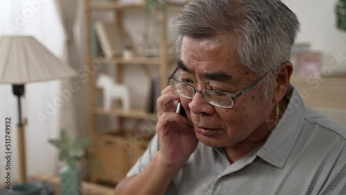 shocked senior asian japanese man having conversation talking on smartphone on sofa. stressed old male hearing bad news by cellphone call at modern home. amazed grandpa fear and upset for mistake