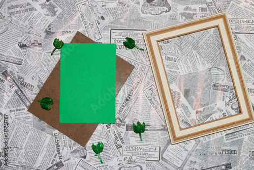 wooden board with green paper as copy space, next to green dried flowers and wooden frame as copy space on newspaper background, creative background, invitation, greeting card