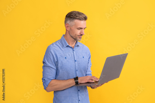 mature man working online on laptop on yellow background, business