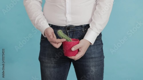 A man in a white shirt and jeans holds a red cactus pot against the background of his groin. The concept of erectile dysfunction in men, prostate disease, close-up photo