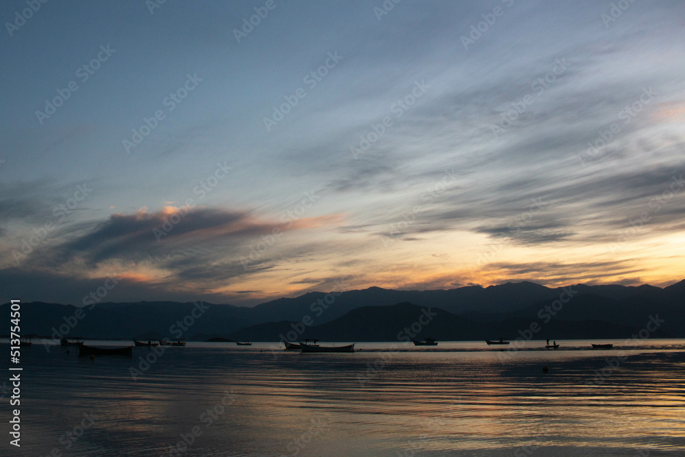 Incredible sunset over the sea, with small boats and the hills in the background, in Caieira da Barra do Sul, 
