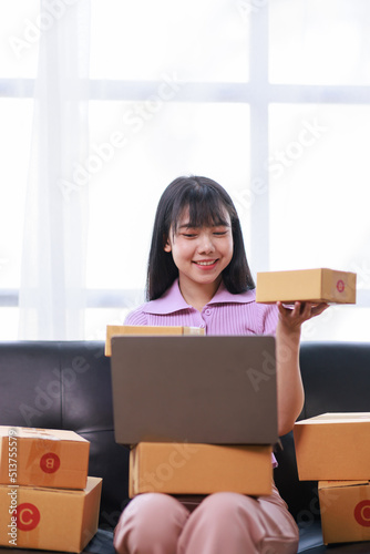 Startup SME small business entrepreneur of freelance using a laptop with box, Asian business woman on sofa check online orders to prepare to pack the boxes sell to customers sme business ideas online.