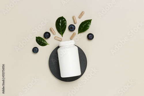Vitamin medical bottle with blueberries, herbal pills and green leaves, top view. Organic supplement for good vision