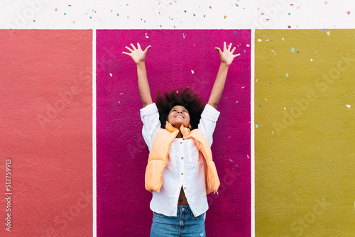 Girl with arms raised throwing confetti standing in front of colorful wall photo