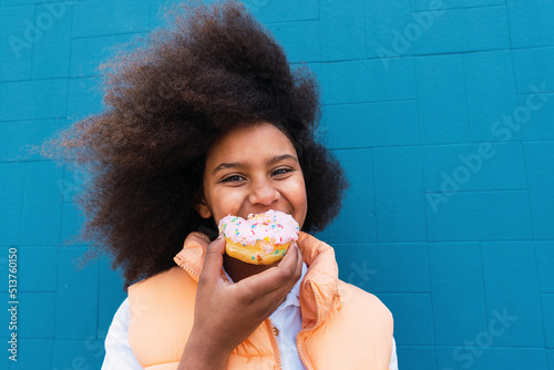 Smiling girl eating doughnut in front of blue wall photo