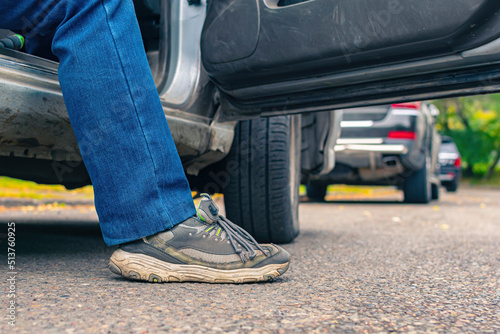 A passenger or driver in jeans and sneakers gets out of the car onto the road, view from below