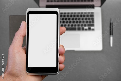 Man holding a smartphone with black screen on office table.