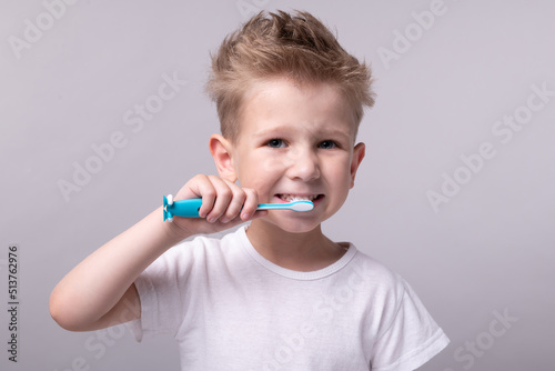 a boy in a white t-shirt brushes his teeth with a toothbrush