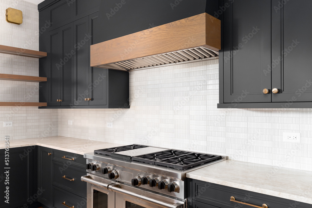 A luxury kitchen with black cabinets, granite counter top, tiled  backsplash, stainless steel appliances, and gold hardware.  Stock-illustration | Adobe Stock