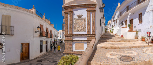 View of whitewashed houses and shoppers on narrow street, Frigiliana, Malaga Province, Andalucia photo