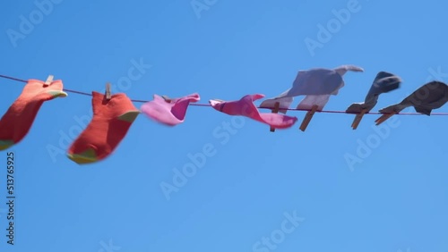 clean colored socks for men and women are dried on a rope with clothespins after washing. the wind shakes bright unisex socks against the blue sky on a sunny summer day. slow motion. photo