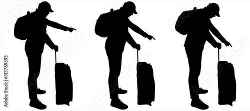 A tourist in a cap and tracksuit with a backpack behind his back, a suitcase on wheels. A young guy of a large physique examines something below and points down with his finger. Side view, profile.