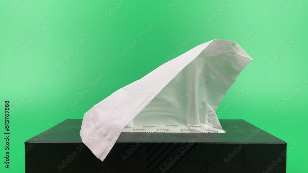 a person's hand pull out a piece of tissue from tissue paper box isolated on green background.