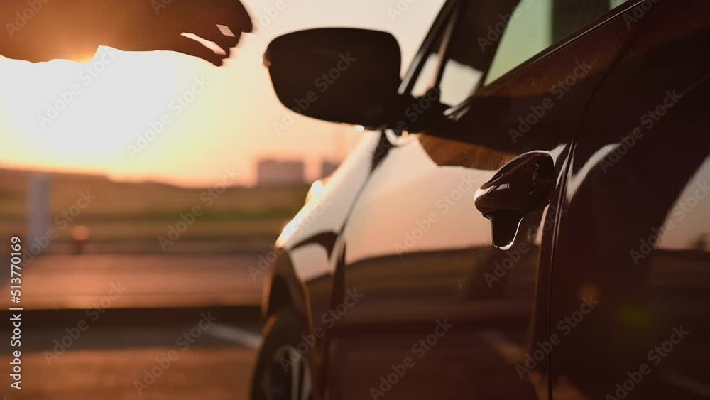 A young attractive girl in light clothes opens the door of red car and gets behind the wheel at sunset. Cinematic slow motion footage with rays of the setting sun. Girl driver, lifestyle, travel