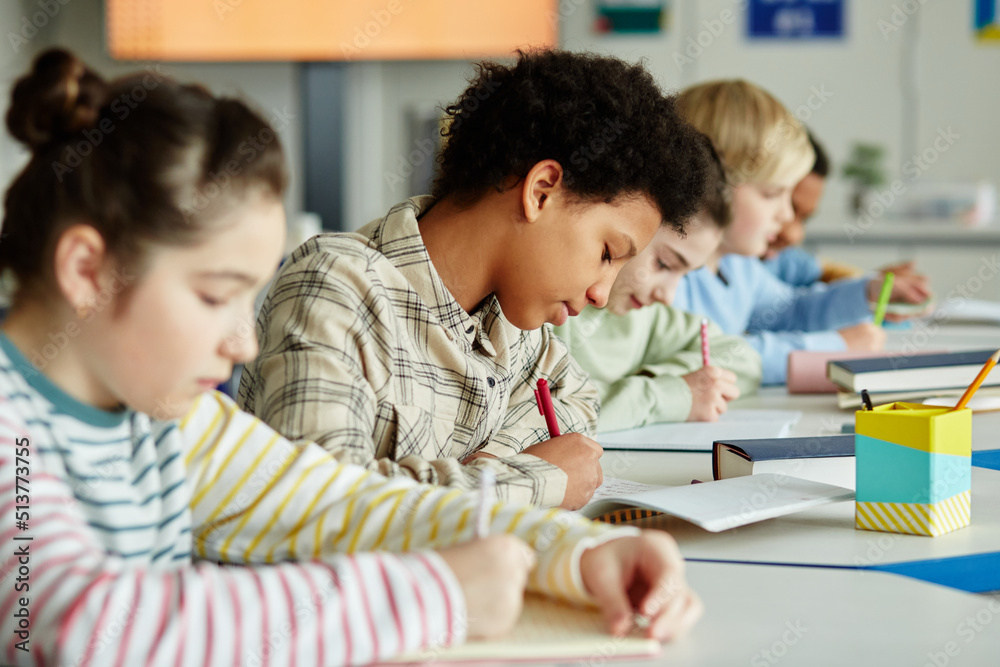 Side view portrait of young black girl taking test in school classroom with group of children sitting in row Side view portrait of young black girl taking test in school classroom with group of children sitting in row