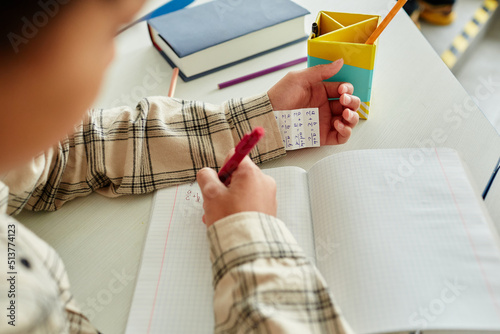 Close up of unrecognizable young boy cheating during test in school and hiding note in sleeve, copy space