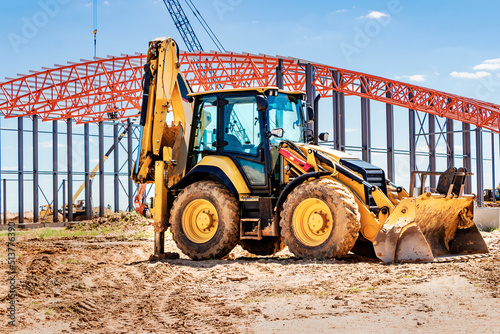 The excavator backfills the pit with the front bucket. Moves soil around the construction site. Close-up. Heavy construction equipment.