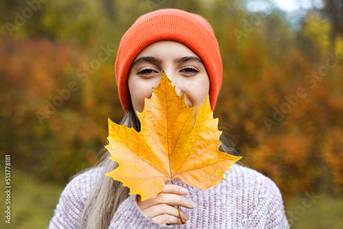 Happy girl with yellow maple leaf. Smiling young woman in autumn park. Portrait