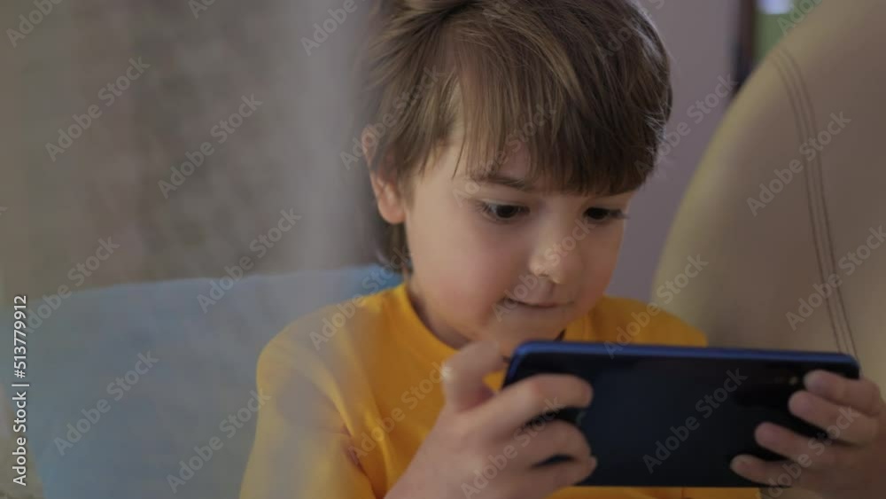 Child Playing Games In Phone at Home Sitting on Couch. Boy Playing Video Game on Mobile Phone. Preschooler Plays Video Game Smartphone on Sofa. Kid Using Phone for Gaming Online Education Social Media Child Playing Games In Phone at Home Sitting on Couch. Boy Playing Video Game on Mobile Phone. Preschooler Plays Video Game Smartphone on Sofa. Kid Using Phone for Gaming Online Education Social Media