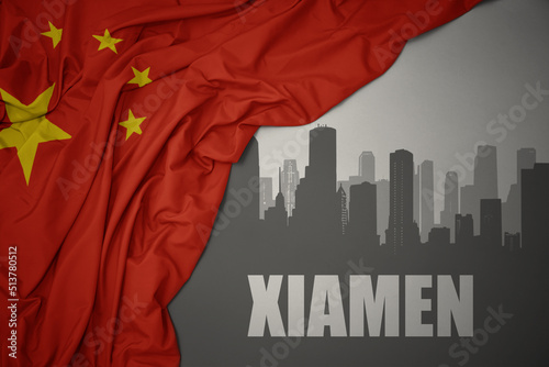 abstract silhouette of the city with text Xiamen near waving national flag of china on a gray background.