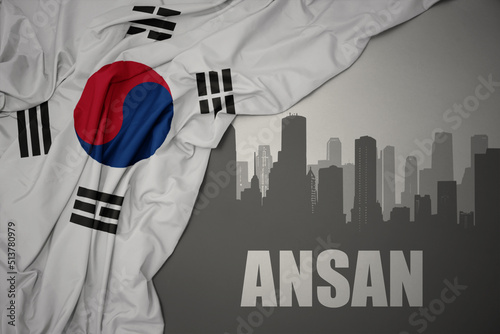 abstract silhouette of the city with text Ansan near waving national flag of south korea on a gray background. photo