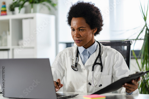 Female doctor working at her office in front of laptop computer, writing a health report