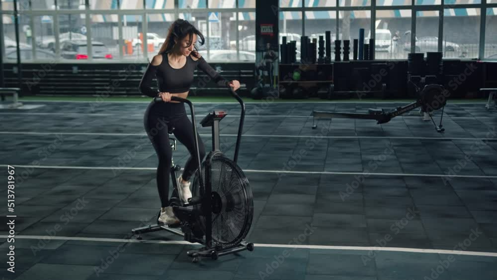 Young female athlete trains cardio on a bicycle with a fan, cardio and endurance training