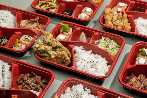 Assorted regular bento BEEF MISONO, TORI TERIYAKI, TONKATSU, SMOKED PORK BELLY, MIXED TEMPURA and KATSUDON with rice, salad, and chopsticks isolated on grey background side view photo