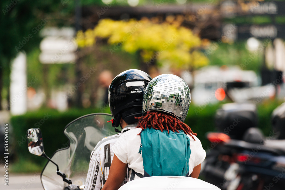 La passagère d'un scooter porte un casque de protection représentant une boule à facettes. La passagère d'un scooter porte un casque de protection représentant une boule à facettes.