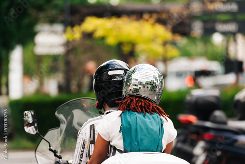 La passagère d'un scooter porte un casque de protection représentant une boule à facettes.