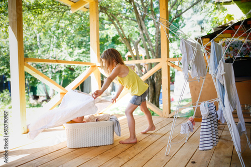 Cute European sibling children hang laundry together on veranda in backyard in summer. Helping children with household routines, relationships and sibling games in family