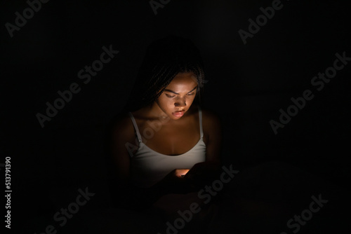 Close up portrait African American woman looking at phone while in bed at night.