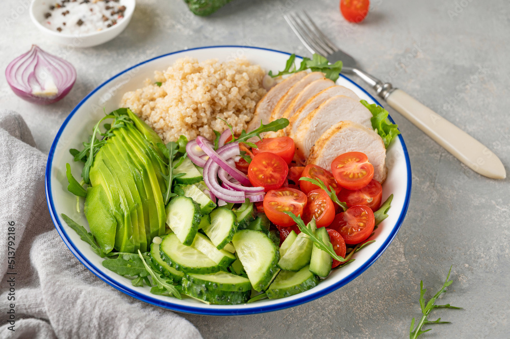 Healthy bowl lunch with grilled chicken, quinoa, avocado, tomatoes, cucumbers and fresh arugula on gray background. Top view. Selective focus. Healthy bowl lunch with grilled chicken, quinoa, avocado, tomatoes, cucumbers and fresh arugula on gray background. Top view. Selective focus.