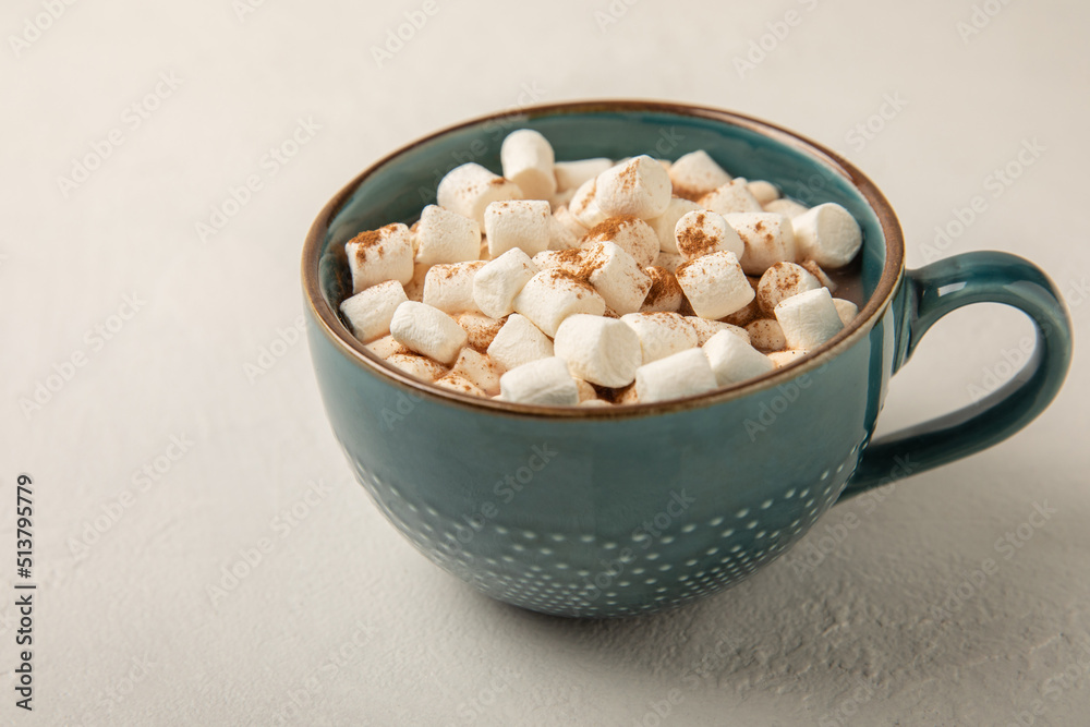 Cocoa drink on white texture background. Hot chocolate with small marshmallows and cinnamon. Winter warming drink concept. Space for copy. Space for text Cocoa drink on white texture background. Hot chocolate with small marshmallows and cinnamon. Winter warming drink concept. Space for copy. Space for text