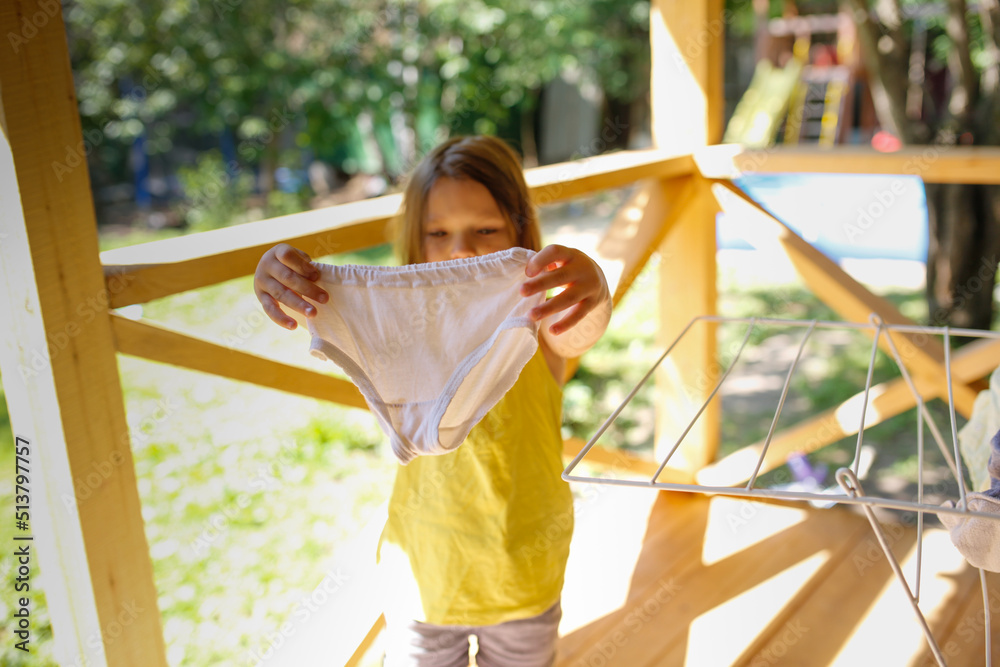 Girl child in T-shirt hangs dry children's panties on dryer