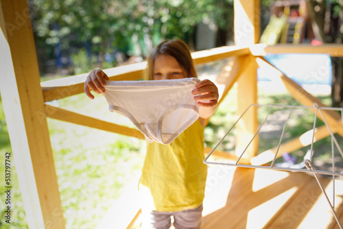 Obraz na płótnie Girl child in T-shirt hangs dry children's panties on dryer outside in summer, c