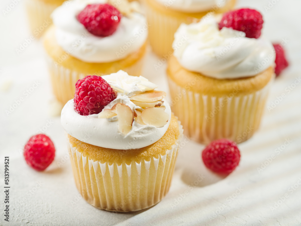 Close-up. Appetizing muffins with cream, decorated with raspberries and almonds on a white background. Cookbook, culinary blog, restaurant and home cooking.
