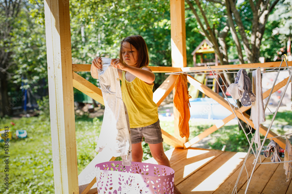 Cute child girl hangs clean linen on dryer outdoor, help with housework and children's duties at home, summer Cute child girl hangs clean linen on dryer outdoor, help with housework and children's duties at home, summer