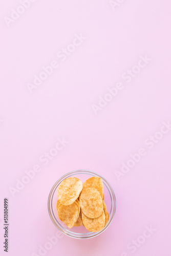 Potato chips in glass bowl on pink background. Fast food.