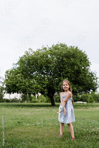 Happy emotional child girl posing outside in the green park. Fashion kid. Smiling toodler girl walking in park.