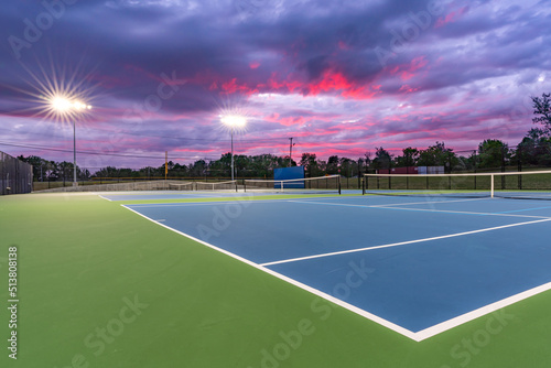 Evening photo of outdoor blue tennis courts with pickleball lines with lights turned on.	 photo