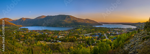 Panoramic view of two Colorado lakes and towns next to them on fall evening with sun setting and moon rising