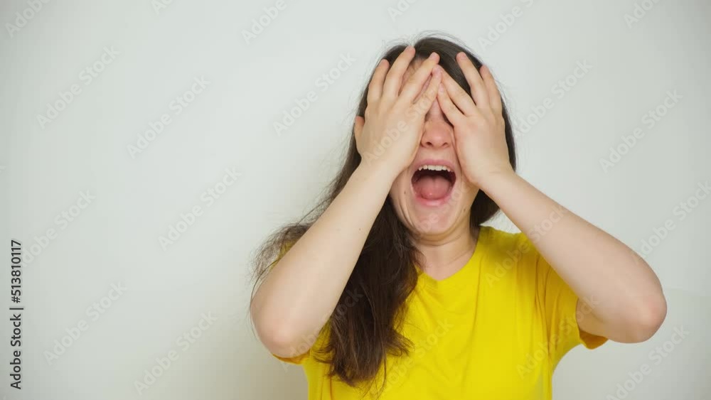 A woman dries her hair with a dryer, looks at her hair and covers her face with her hands screaming.