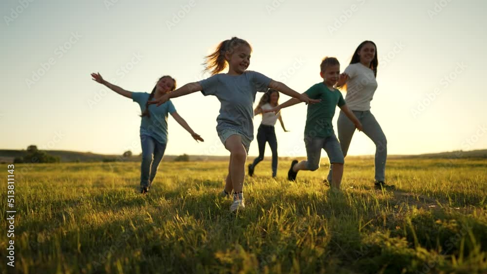 Happy family of children in summer outdoors.Children run together on grass in meadow.Silhouette of group of people playing in field.Boys and girls have fun run in the park at sunset.The Joy of Friends Happy family of children in summer outdoors.Children run together on grass in meadow.Silhouette of group of people playing in field.Boys and girls have fun run in the park at sunset.The Joy of Friends
