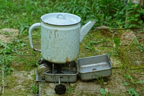 a metal old gasoline primus stove in an iron box for boiling water in an iron kettle in nature lies on old bricks in the summer on the street