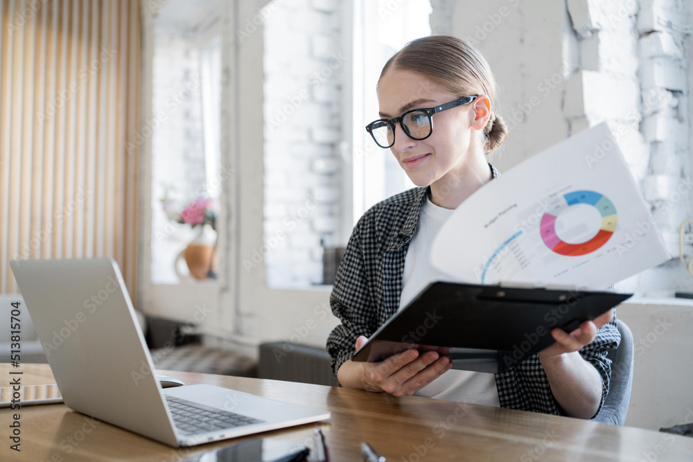 The manager, a woman with glasses, works, uses a laptop, makes a report to the company on finances The manager, a woman with glasses, works, uses a laptop, makes a report to the company on finances