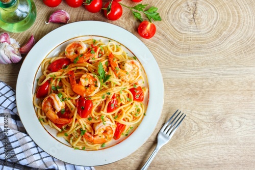 Italian Traditional Dish"Spaghetti con gamberi",spaghetti with prawns or shrimps,cherry tomatoes,olive oil,garlics,parsley,salt and peppers on plate with wooden background.Top view