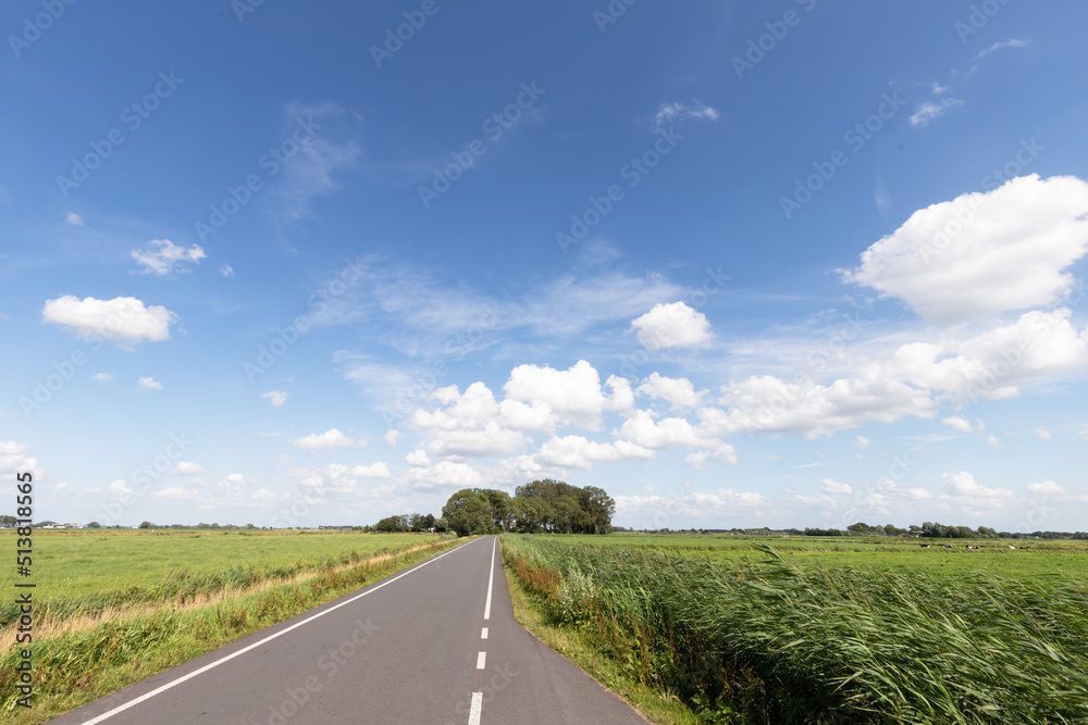 Clouds, a blue sky and a lot of wind above a country road in the rural polder landscape in the Netherlands.